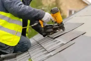 Person installing shingles on a roof with a nail gun, representing the best roofing company San Diego.