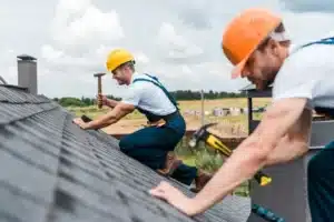 Best roofing company oceanside team working on a shingled roof with safety helmets and hammers.
